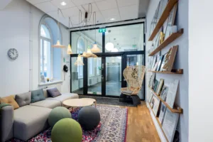 Interiör med sittmöbler, runda bollar som fotpallar, hyllor med böcker och stora fönster som släpper in ljus.