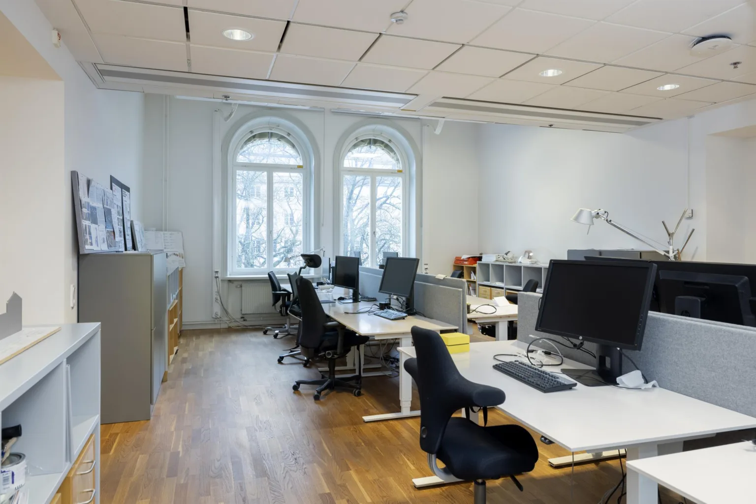 Ett ljust kontor med skrivbord, datorer, kontorsstolar och stora fönster.