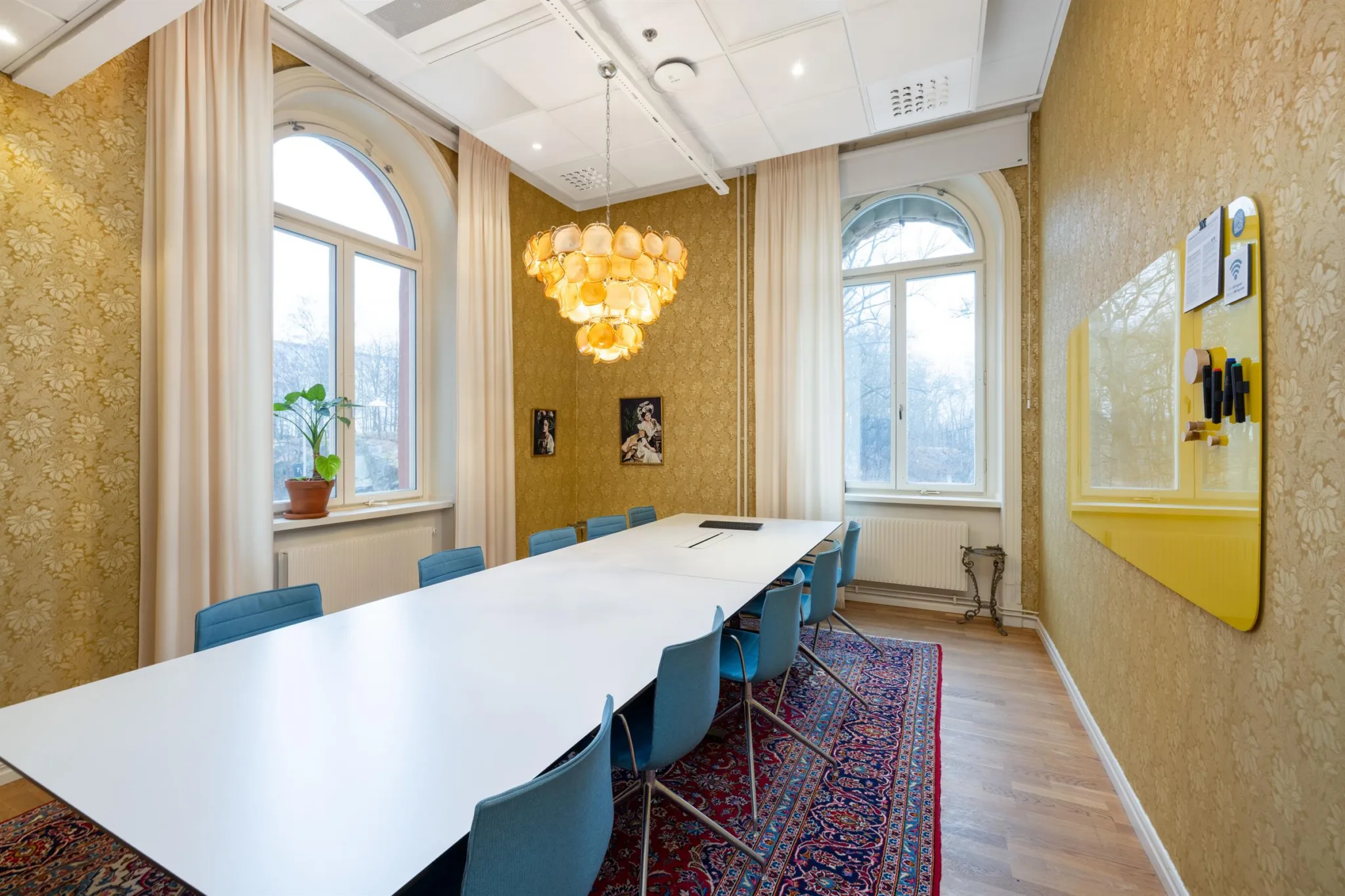Ett konferensrum med ett långt bord, blå stolar, en ljuskrona och stora fönster med dagsljus.