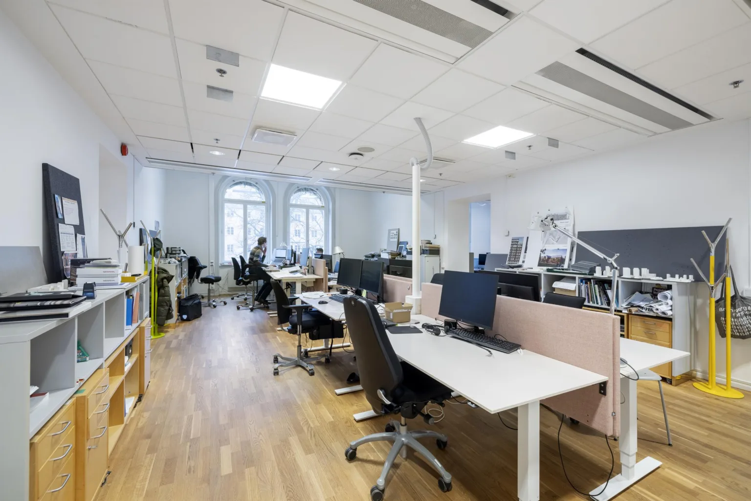 Ett ljust kontor med skrivbord, datorer, stolar och stora fönster.
