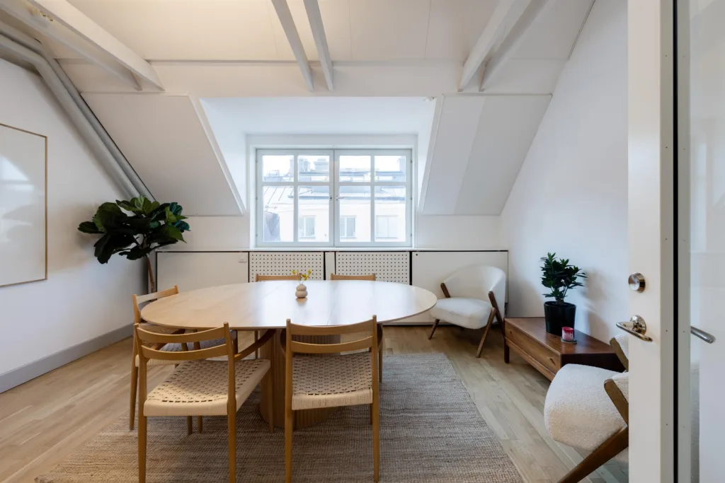 2. Ett ljust mötesrum med ett stort ovalt bord och trästolar, samt växter och fönster.