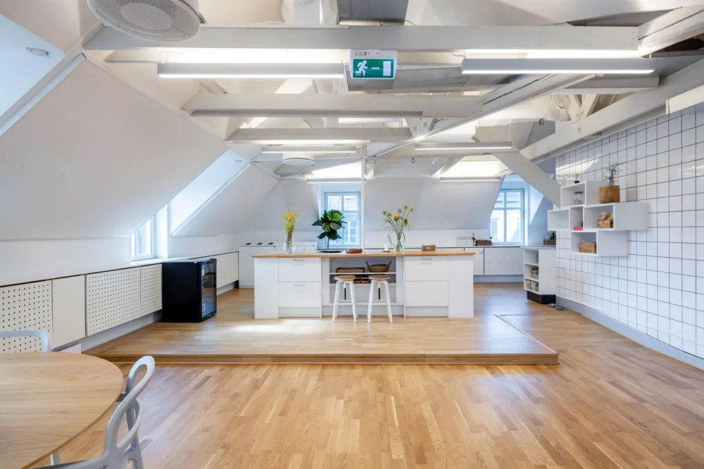 4. Ett modernt kök med stora bänkar, vita skåp, blommor och barstolar på en upphöjd plattform.