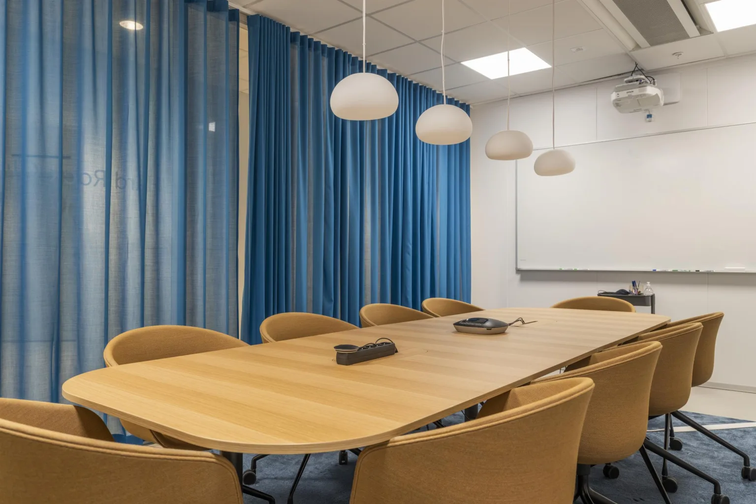Ett konferensrum med blå gardiner, ljusa stolar, ett långt bord och vita taklampor.