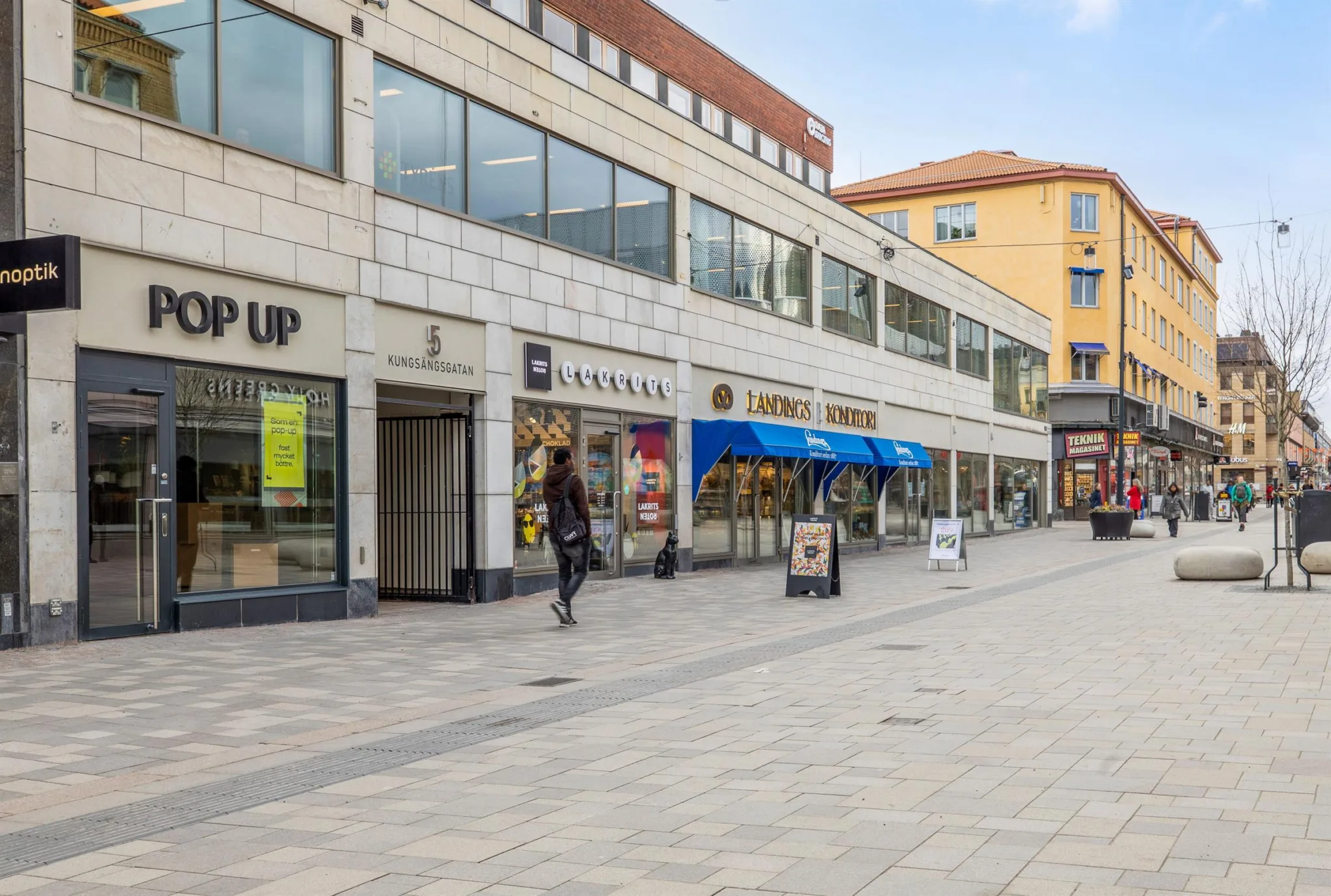 En stadsgata med affärer, skyltar och människor som promenerar.