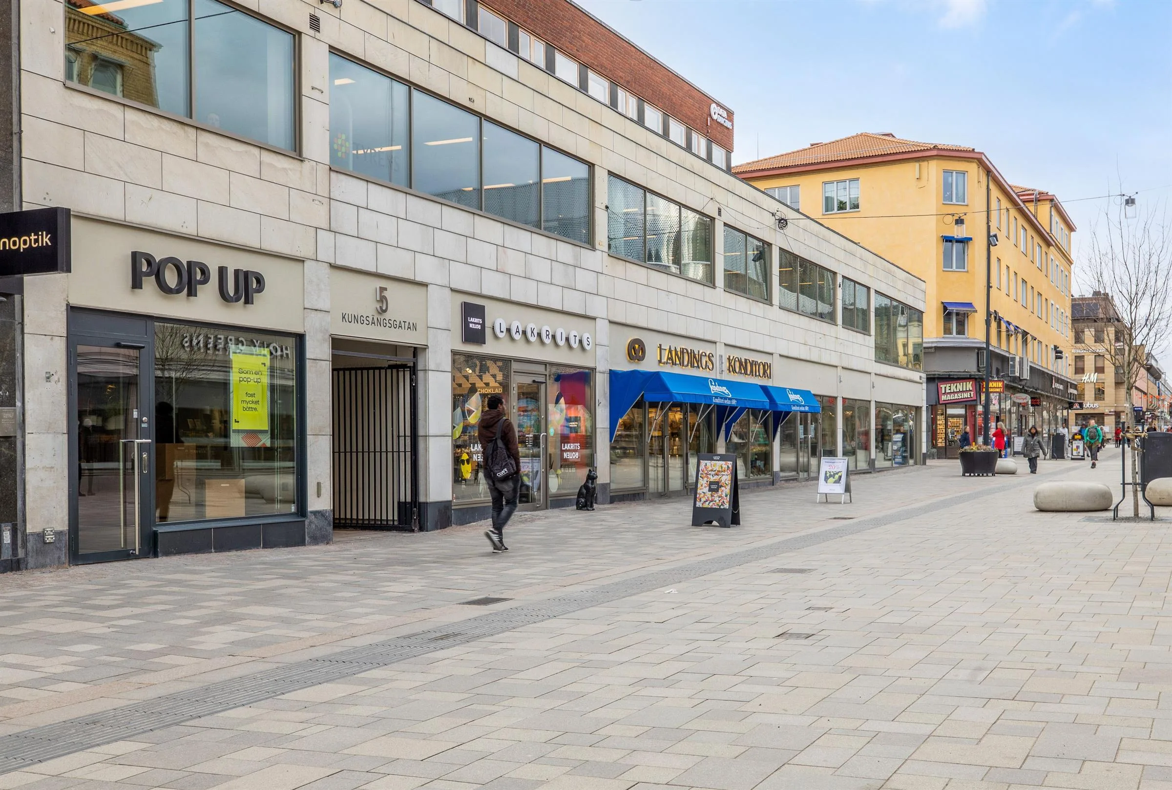En stadsgata med affärer, skyltar och människor som promenerar.