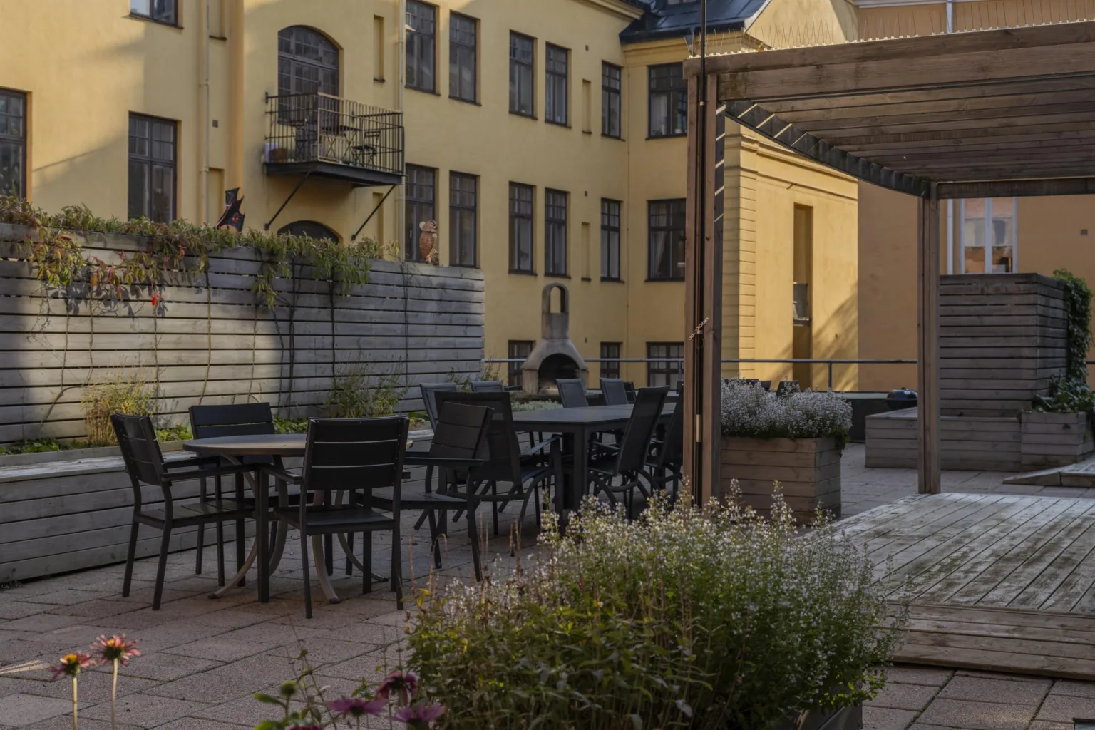 En innergård med gula väggar, utomhusbord, växter och pergola.