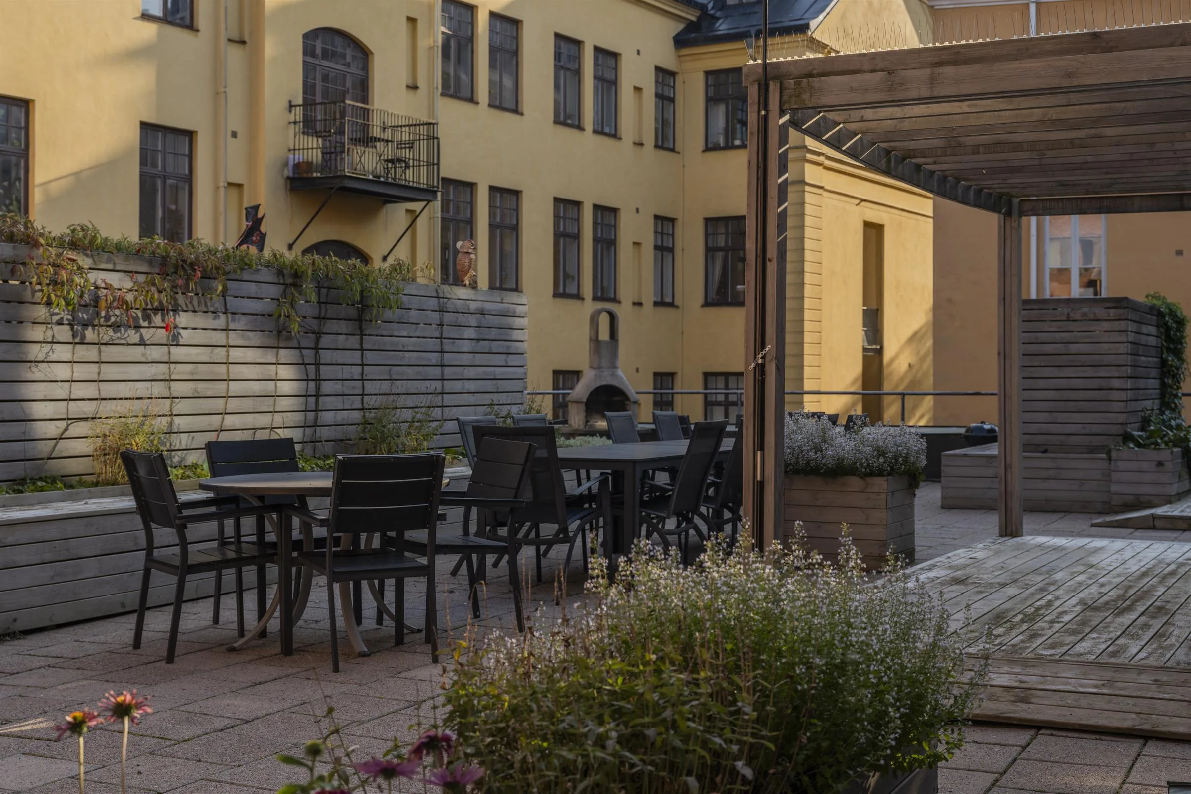 En innergård med gula väggar, utomhusbord, växter och pergola.