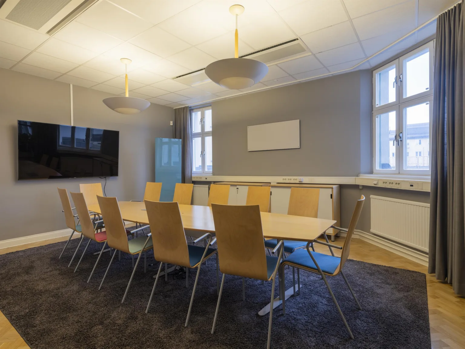 Ett konferensrum med ett stort bord, tio trästolar och en väggmonterad TV.
