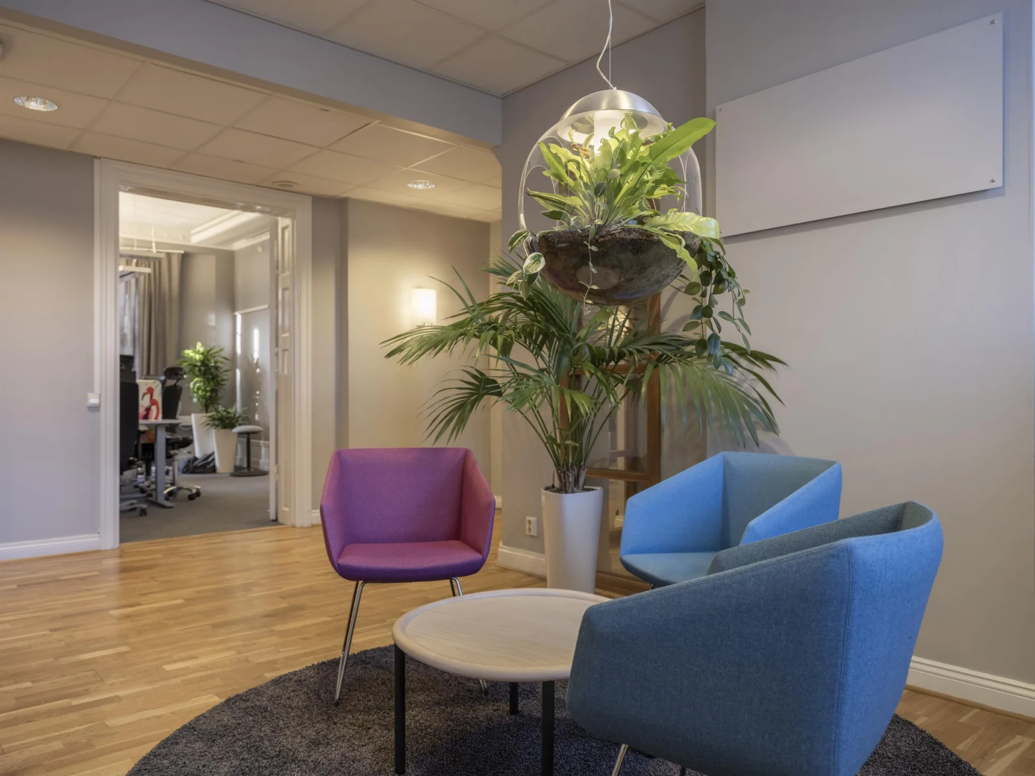 En lounge med färgglada fåtöljer, runda bord och hängande växtdekorationer.