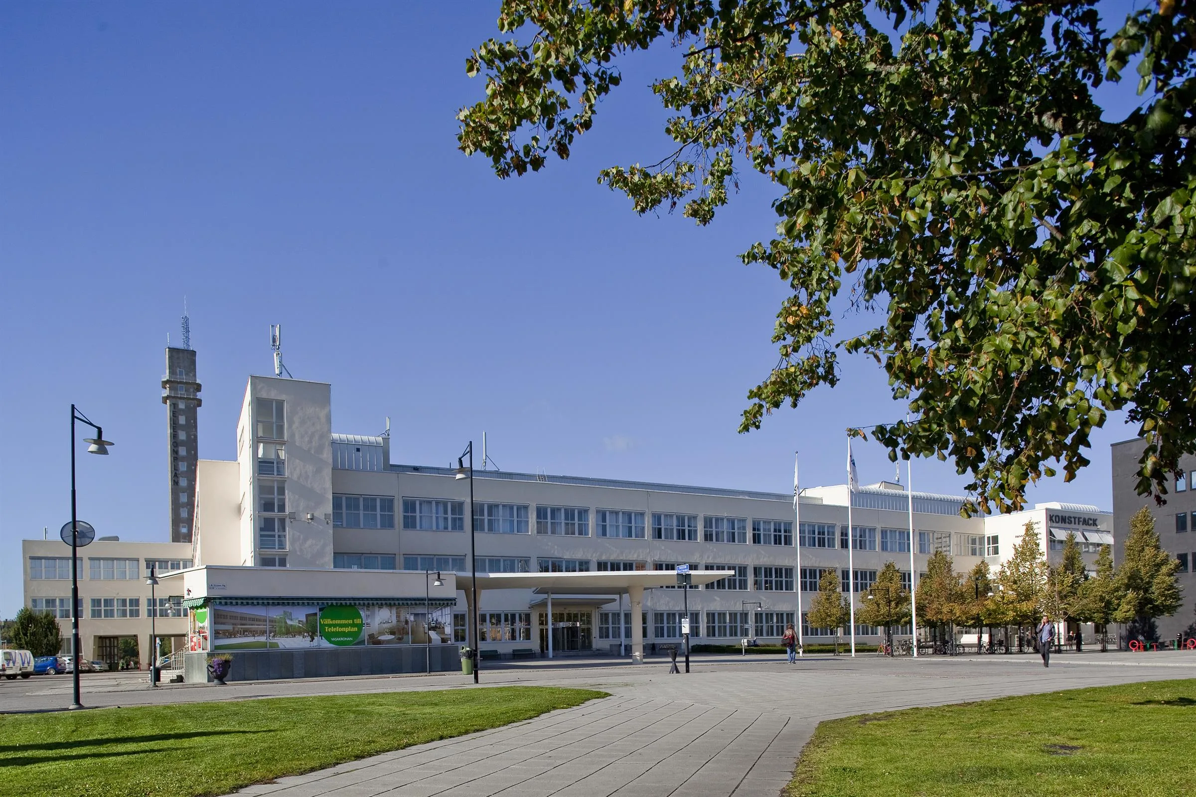 En modern byggnad med vit fasad omgiven av gröna träd, med en gångväg i förgrunden.