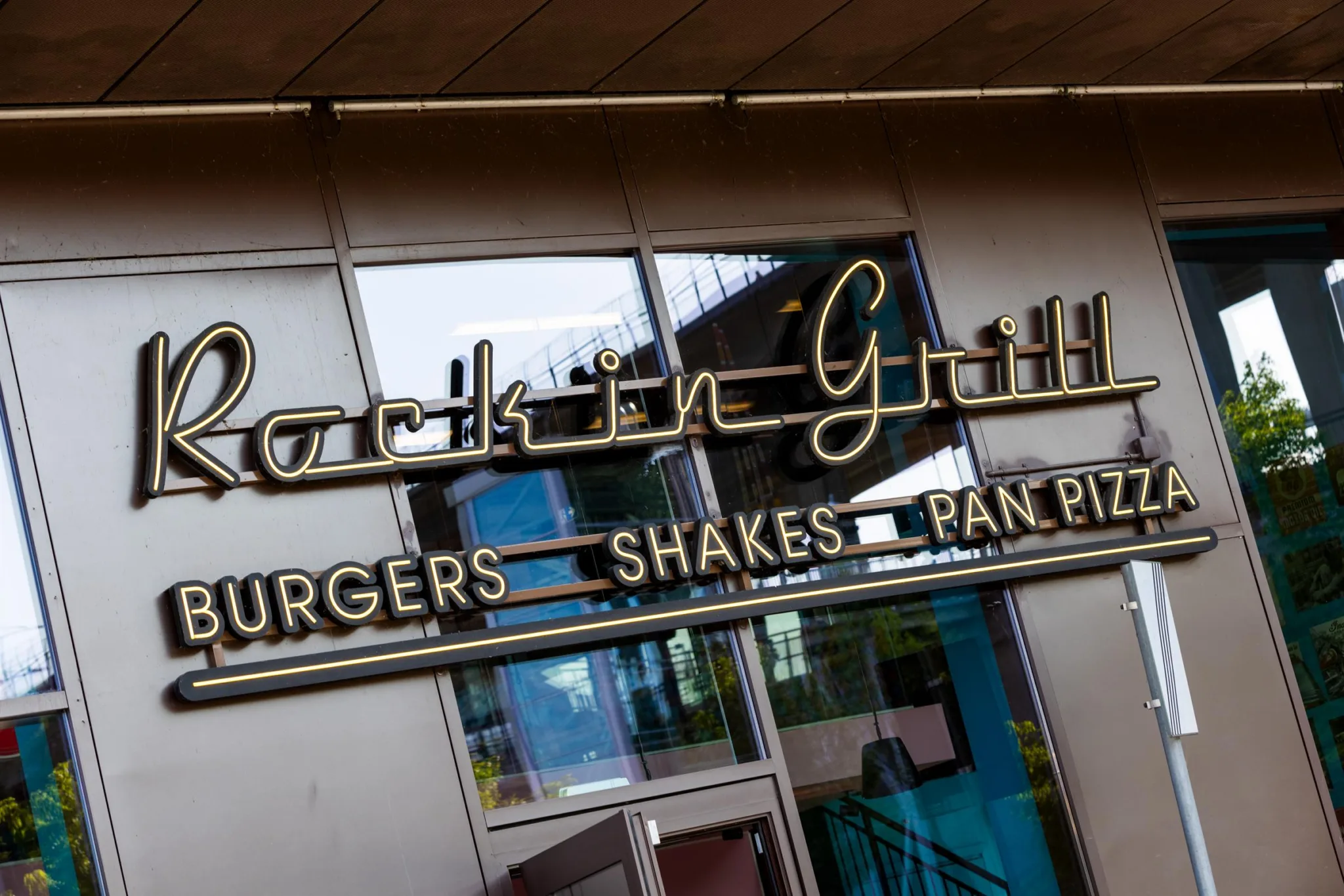 3. En skylt med texten "Parkin Grill Burgers Shakes Pan Pizza" framför en glasfasad.
