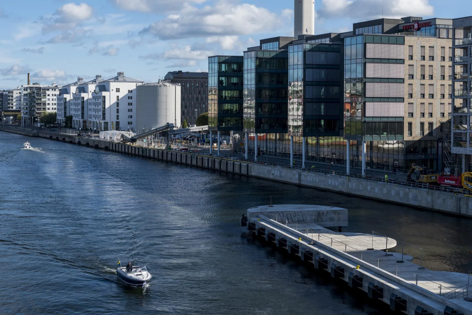1. En båt kör på en bred kanal omgiven av moderna byggnader och en kaj.