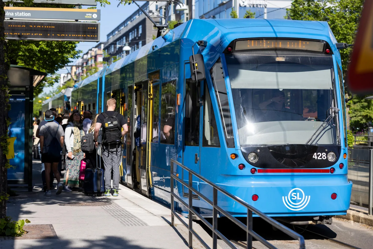 En blå spårvagn på en hållplats där människor går av och på.