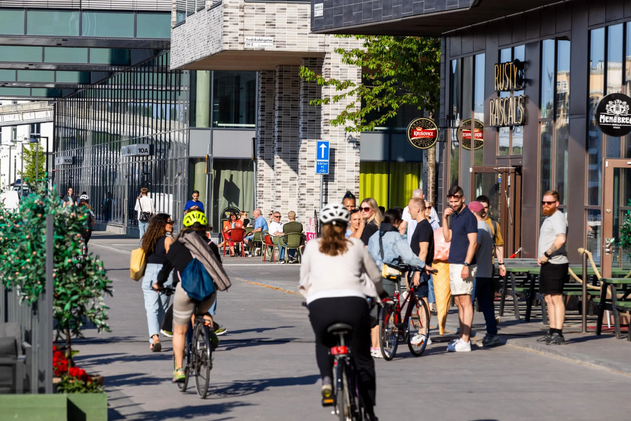4. Människor cyklar och promenerar på en gata omgiven av moderna byggnader och butiker.