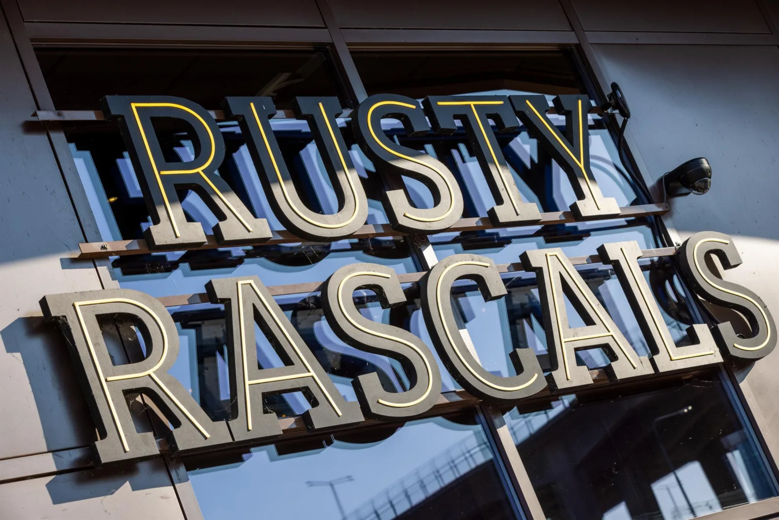 En närbild av en skylt med texten "RUSTY RASCAL" i guldfärgade bokstäver.