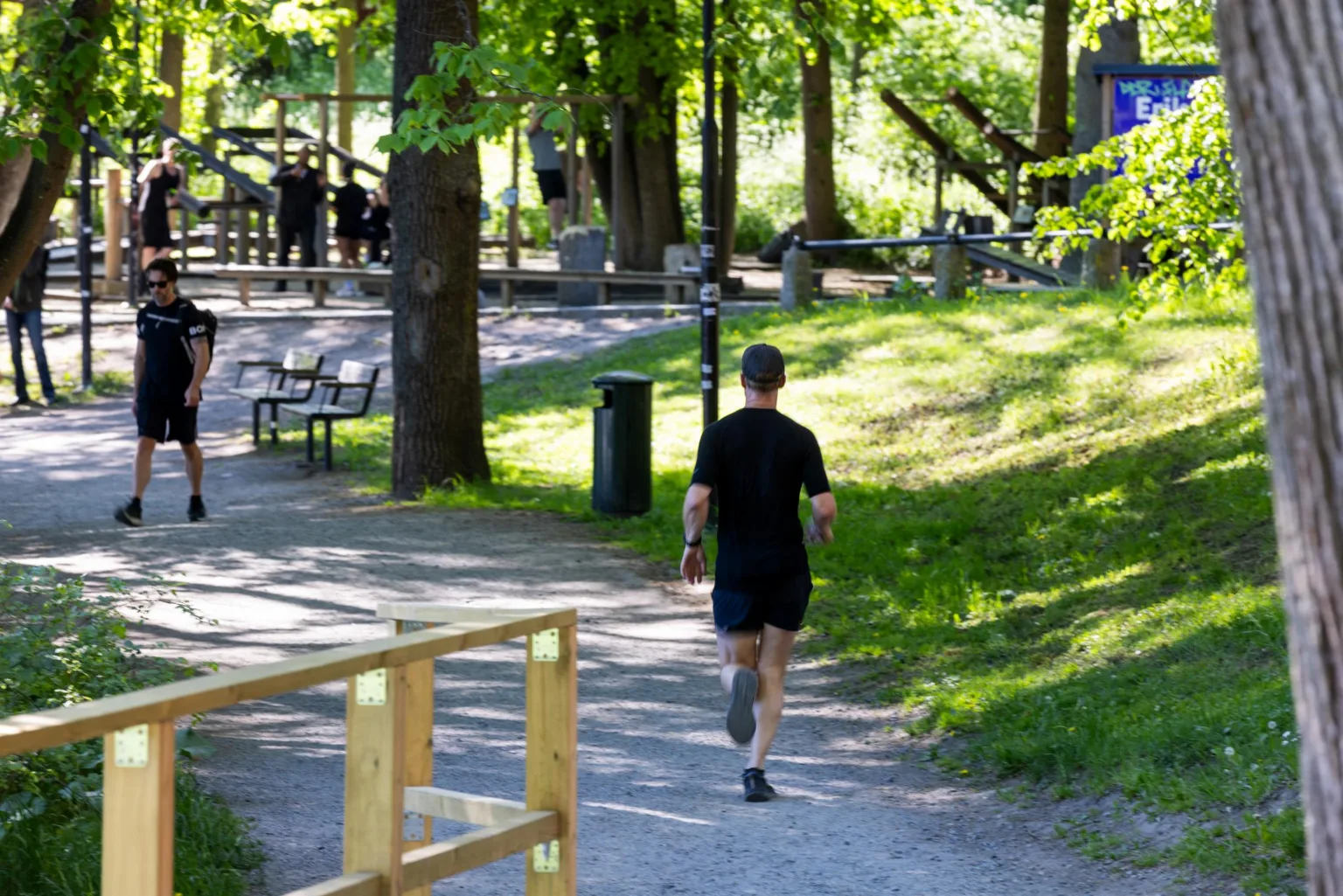 En person joggar på en solig gångväg omgiven av träd och grönska.