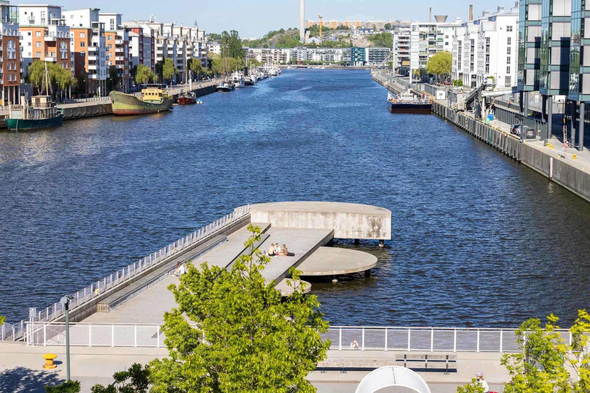 En bred kanal omgiven av moderna byggnader och båtar, med en gångbro i förgrunden.