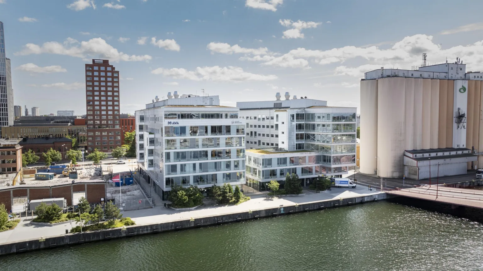 3. Två vita kontorsbyggnader vid en kanal, omgivna av träd och parkeringsytor.