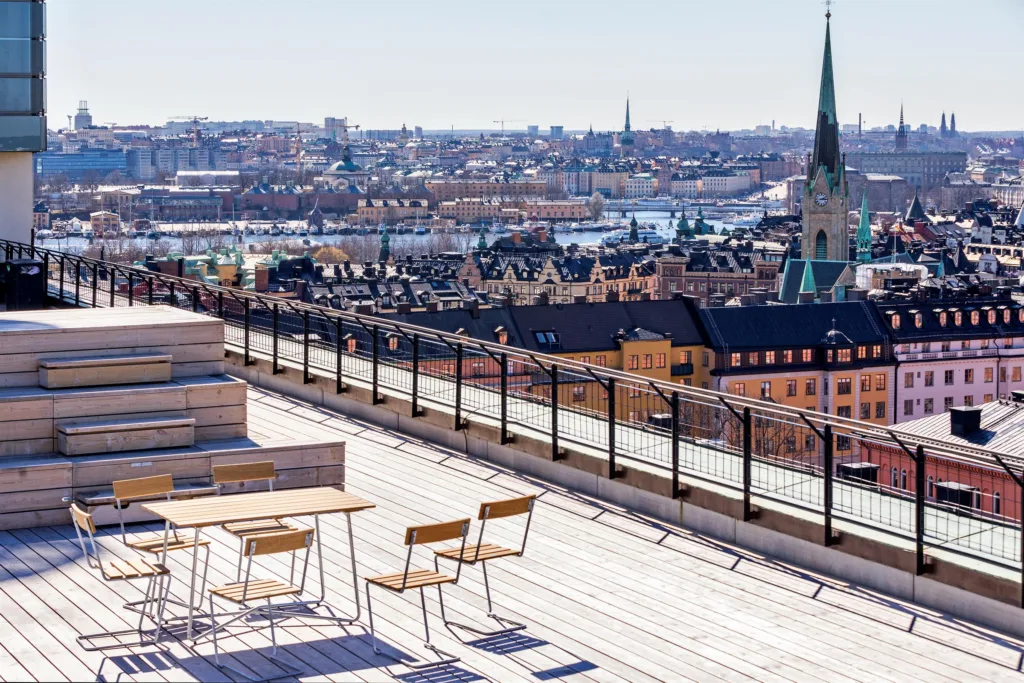 En takterrass med bord och stolar med utsikt över Stockholm, inklusive kyrkspiror och hustak.