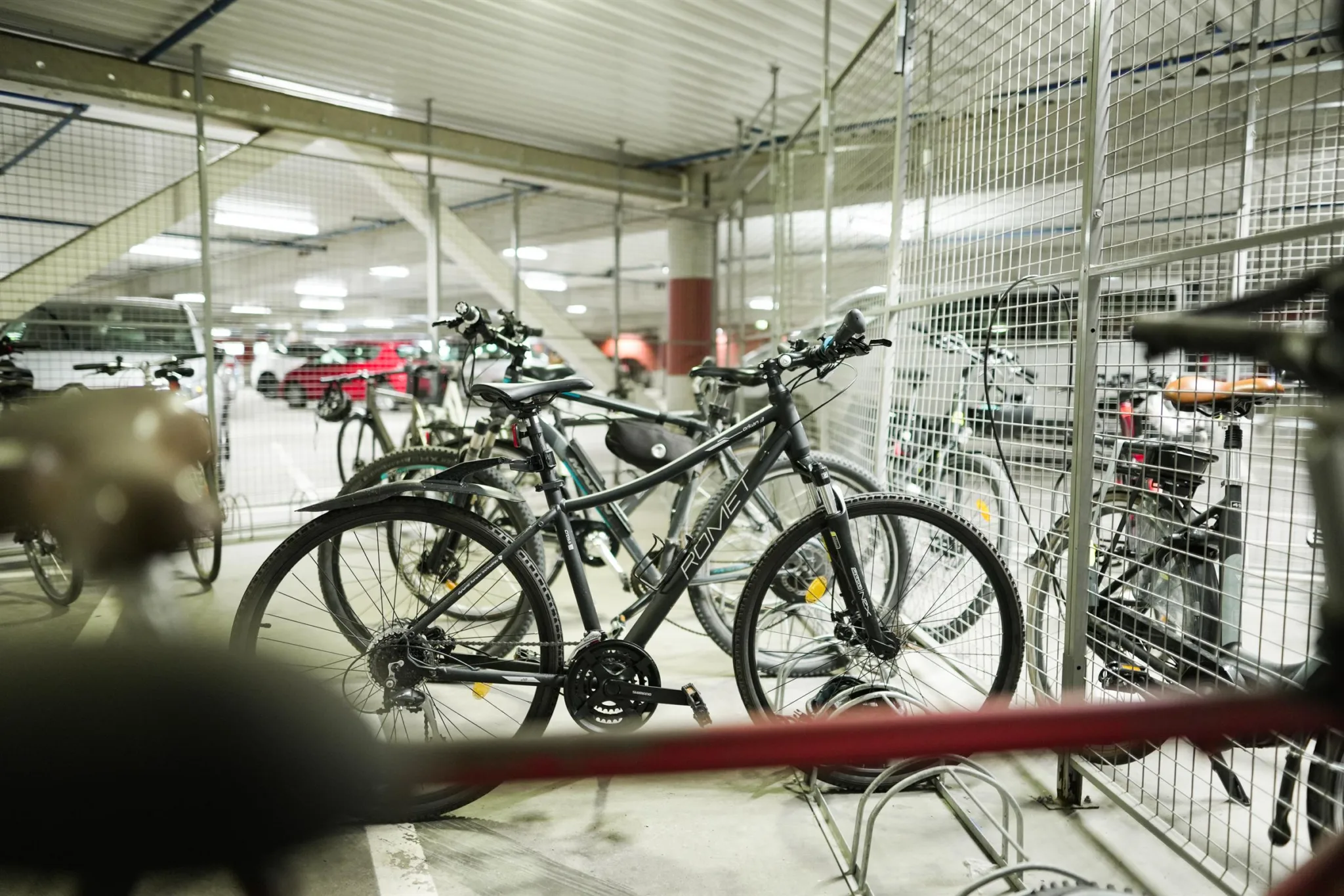 Cyklar parkerade i ett inomhuscykelställ med metallnät runtom.