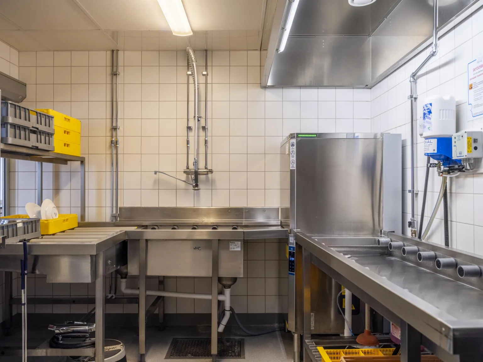 Ett industriellt kök med diskbänkar, rostfritt stål och kaklade väggar.
