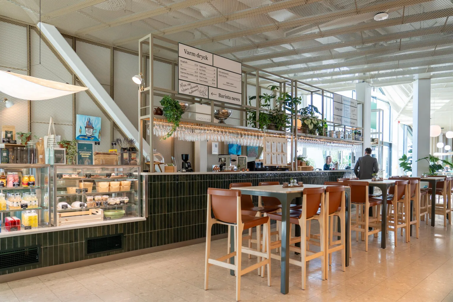 1. En modern kafé med höga stolar, gröna växter och meny ovanför disken.