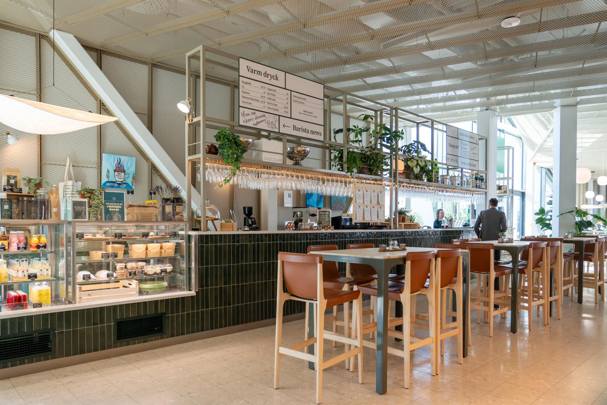 1. En modern kafé med höga stolar, gröna växter och meny ovanför disken.