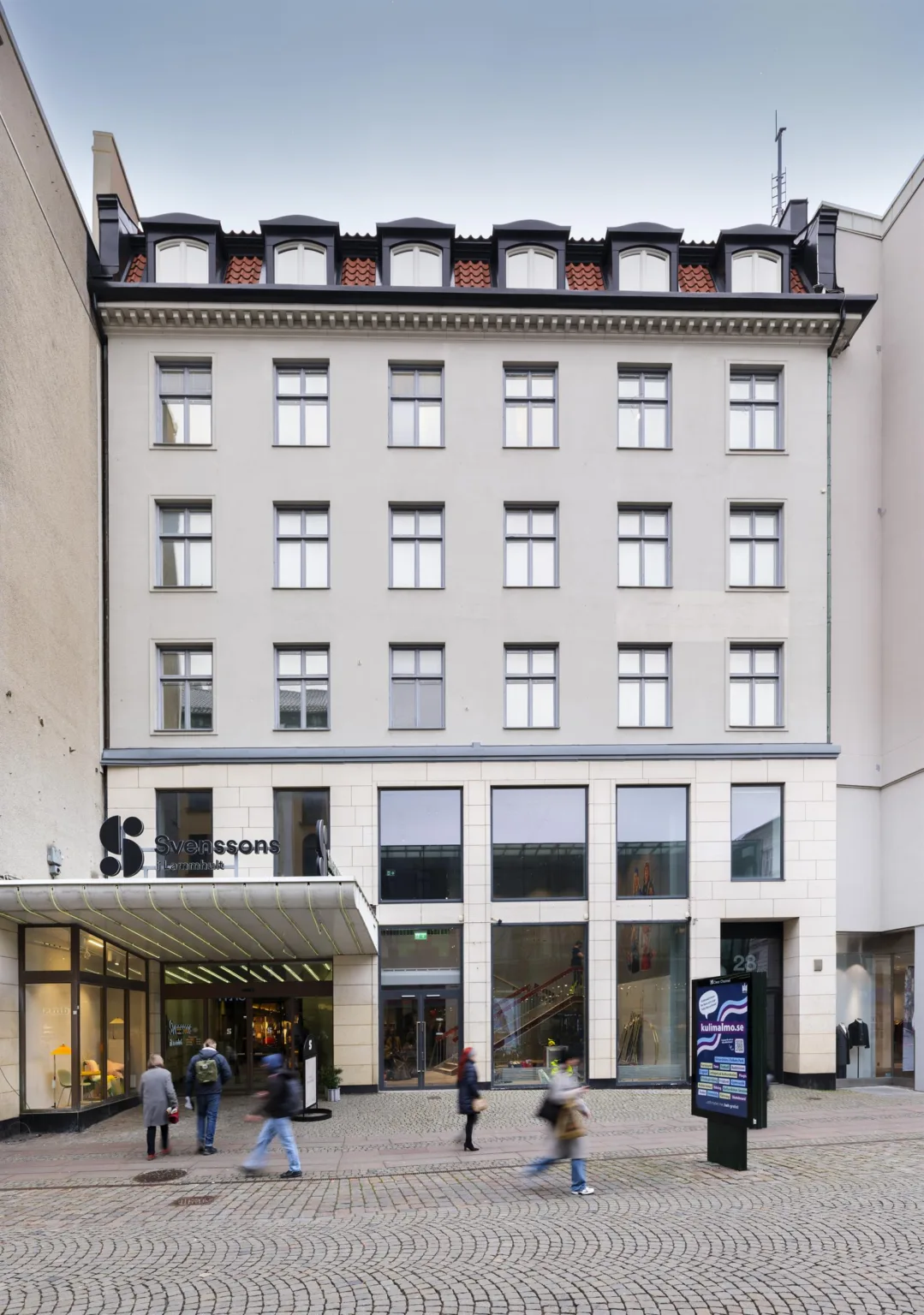 Flerbostadshus med grå fasad, många fönster, och entréområde med glaspartier.