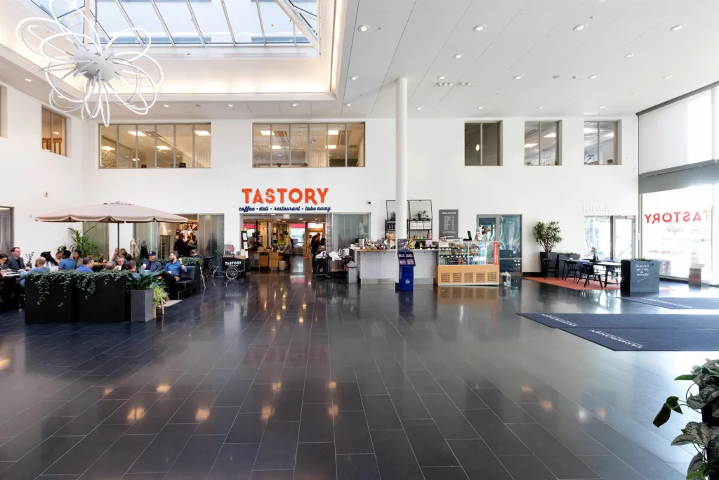 2. Ett modernt och ljust inomhusutrymme med skylt "TASTORY" ovanför en restaurang och sittplatser.