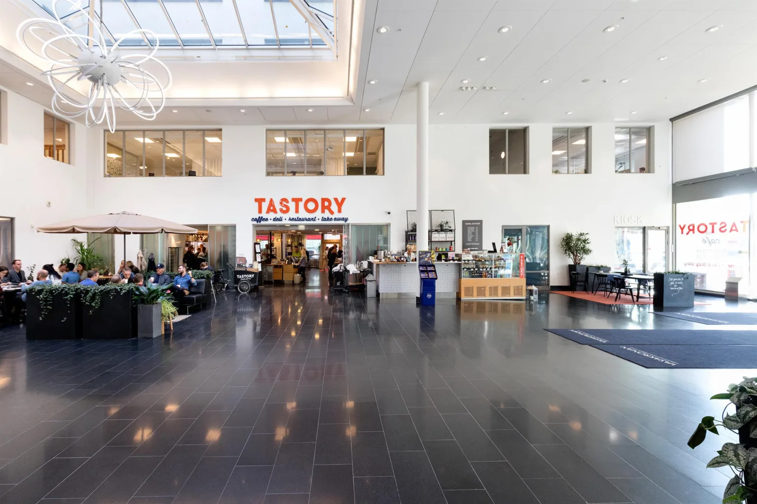 2. Ett modernt och ljust inomhusutrymme med skylt "TASTORY" ovanför en restaurang och sittplatser.