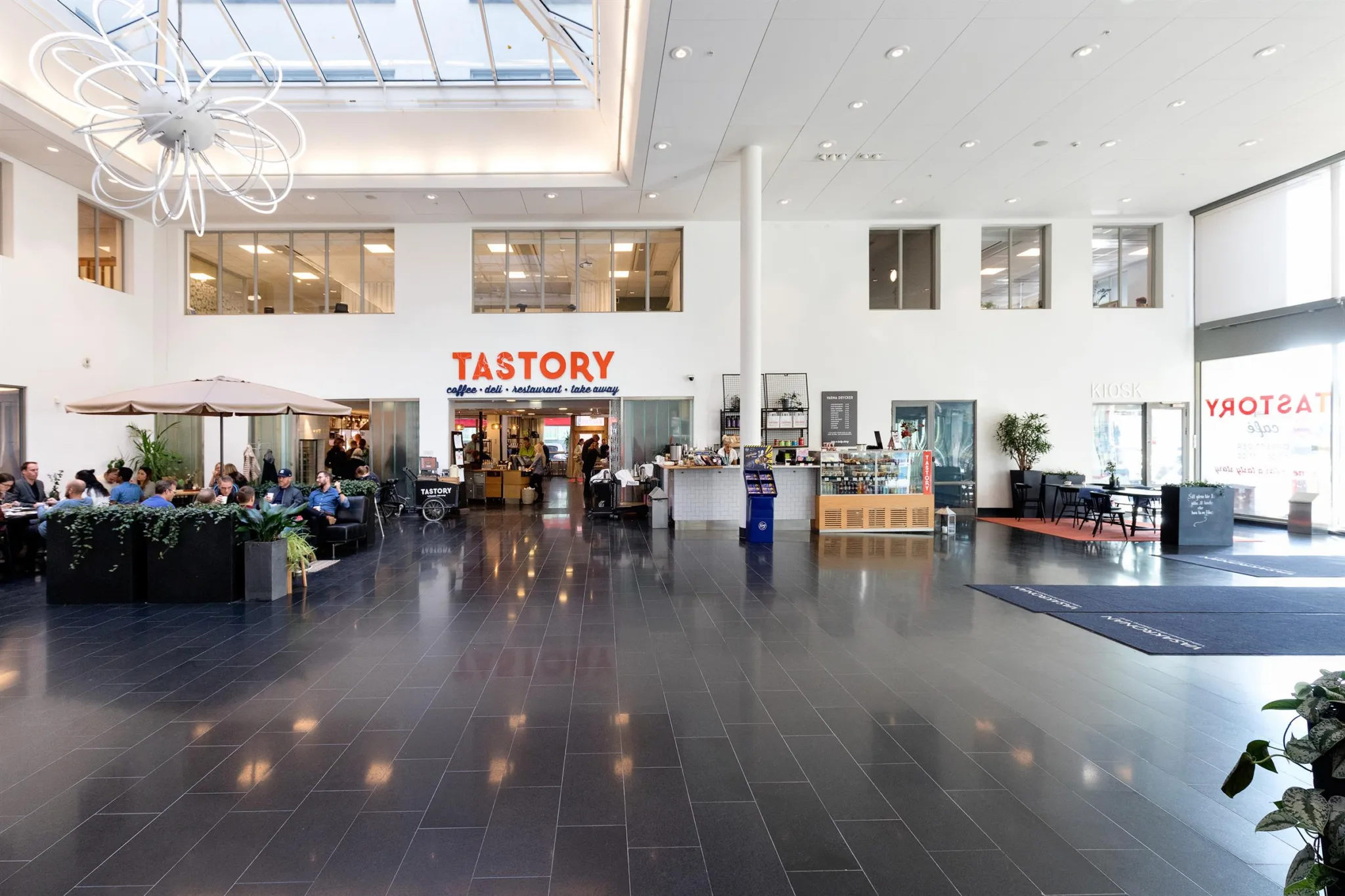 2. Ett modernt och ljust inomhusutrymme med skylt "TASTORY" ovanför en restaurang och sittplatser.