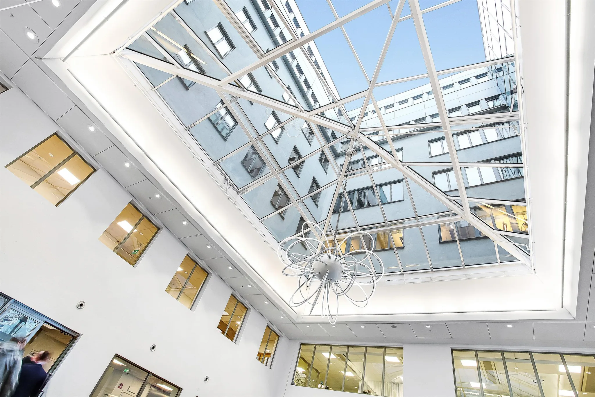 Ett modernt atrium med höga fönster, vit interiör och ett glastak som släpper in dagsljus.