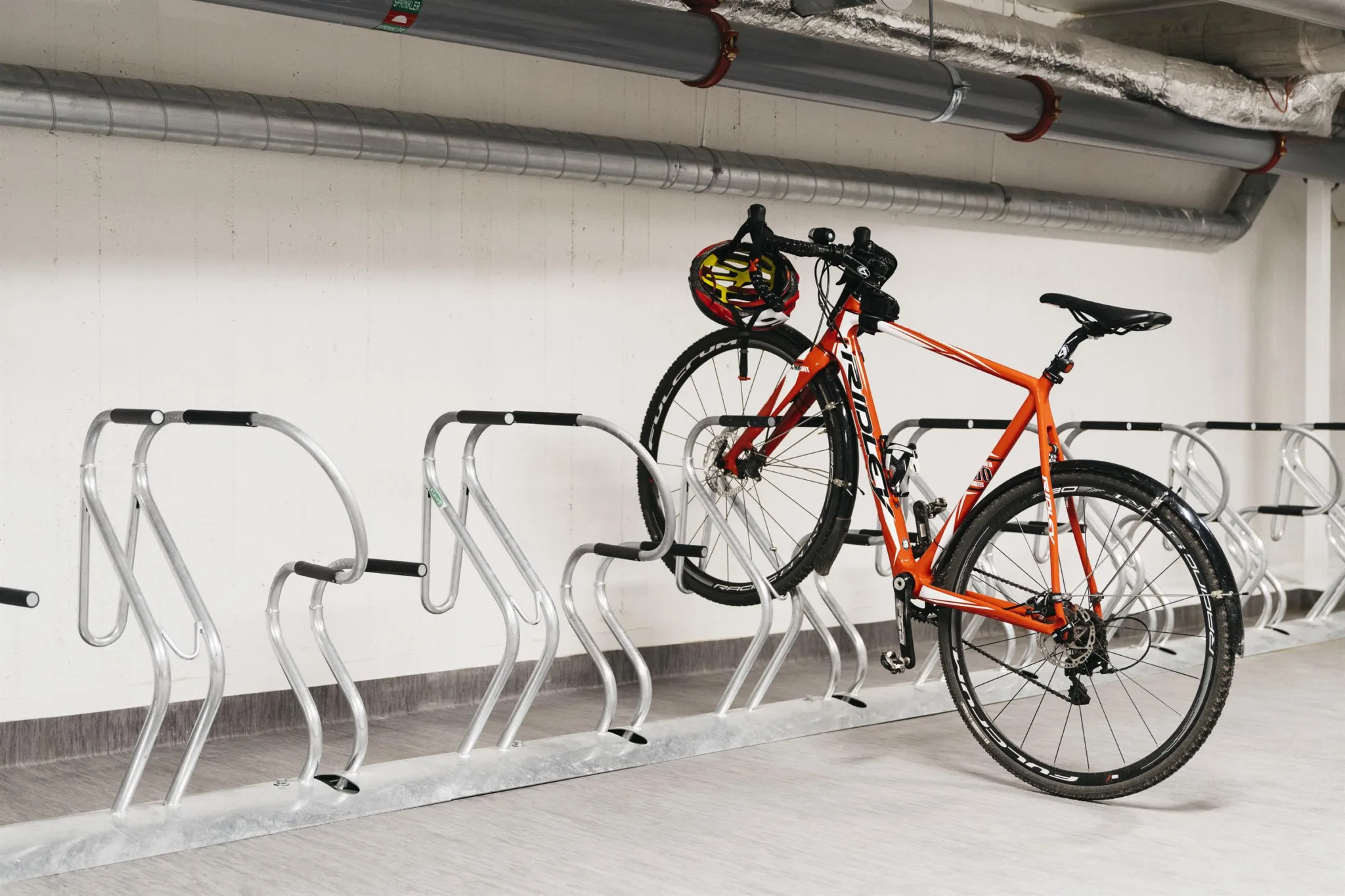 Orange cykel parkerad i en metallställning i ett garage.