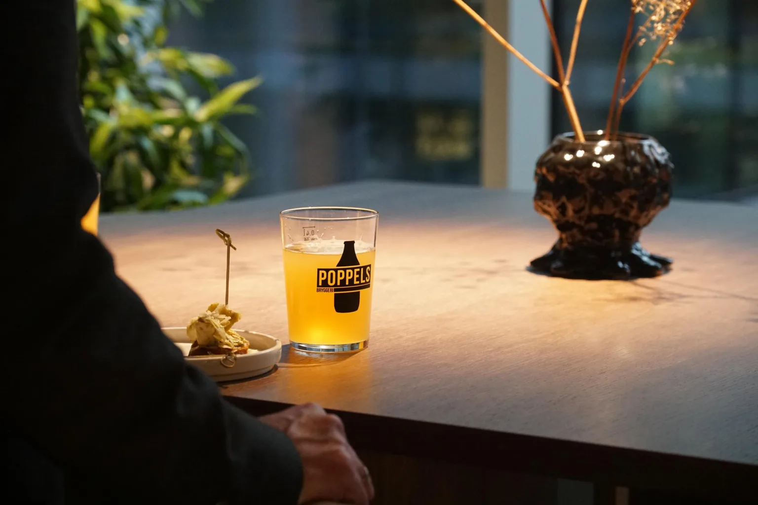 2. Ett glas med gul dryck och logotypen "Norr" på ett bord bredvid en tallrik med mat.