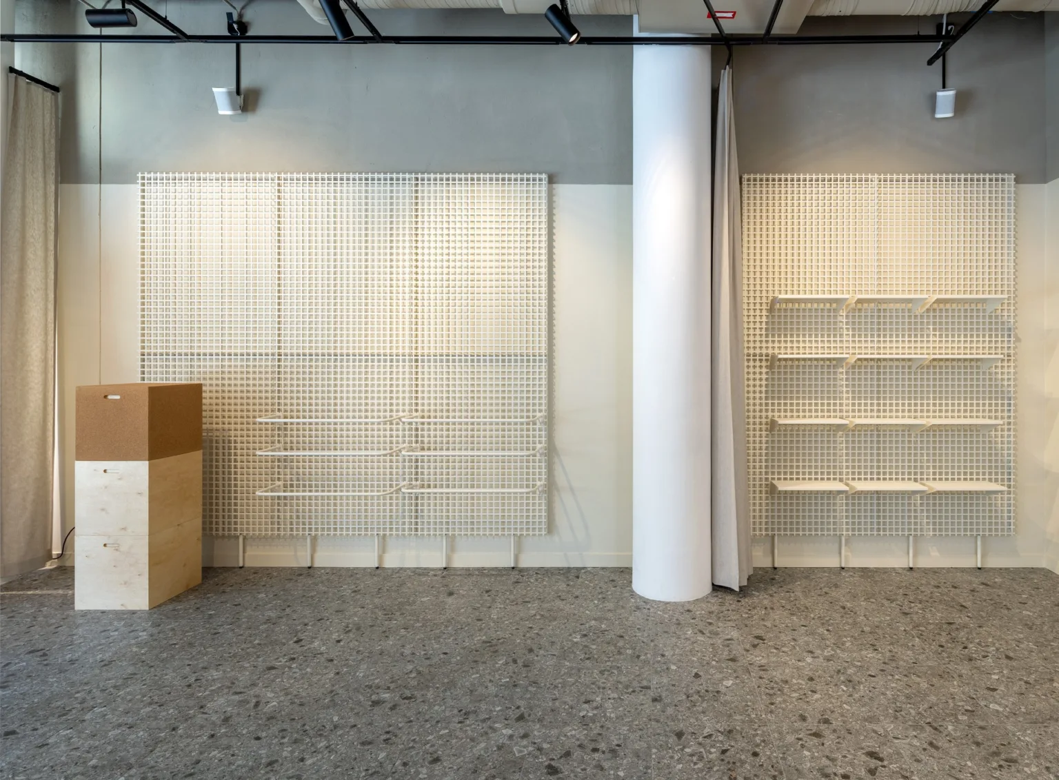 Inre väggar av butik med vita hyllor och en pelare, golvet är grått och inredningen minimalistisk.