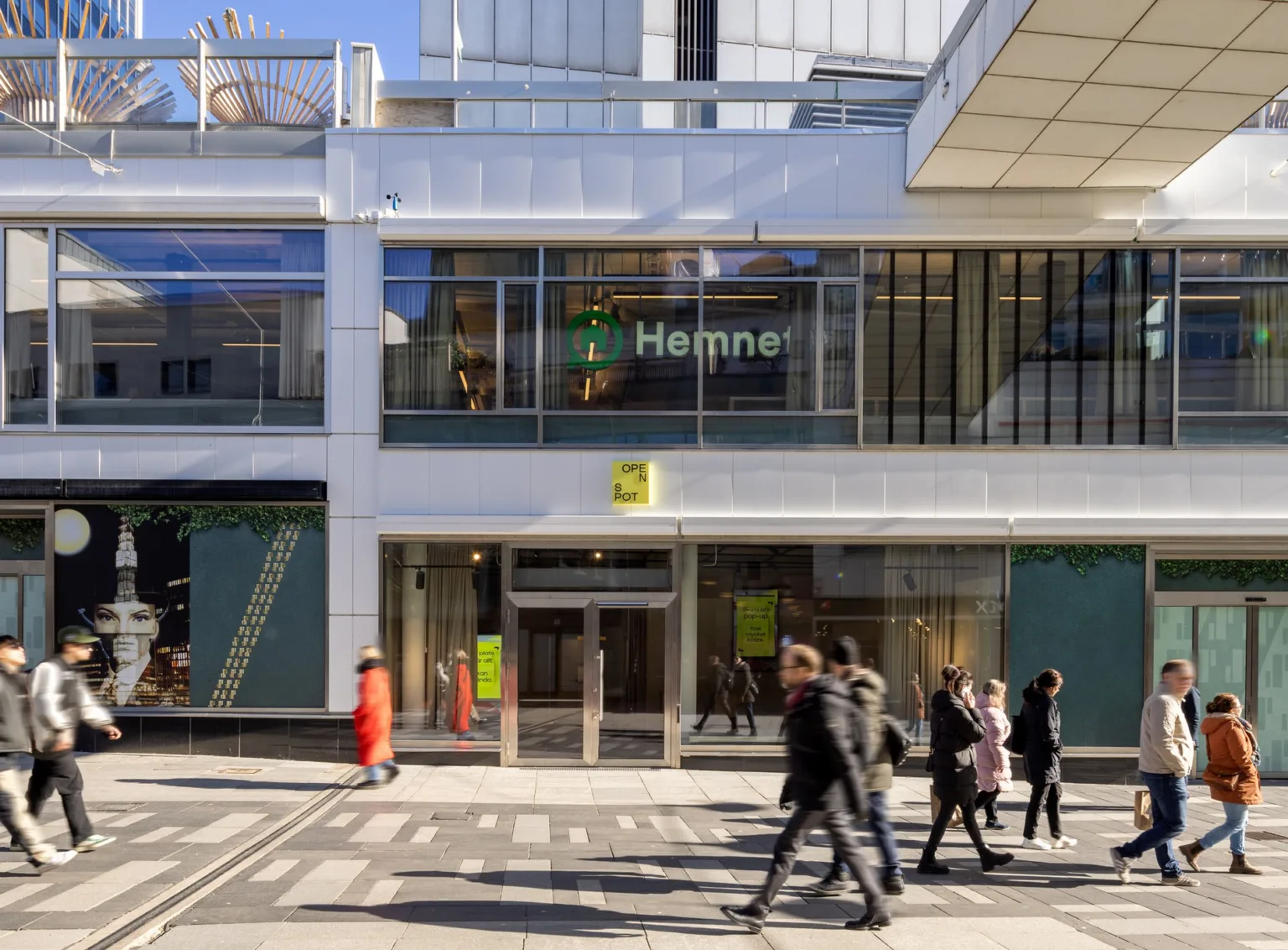 Utomhusbild av byggnad med "Hemnet"-skylt, människor som går på gatan framför och glasfasad.