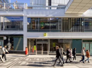 Utomhusbild av byggnad med "Hemnet"-skylt, människor som går på gatan framför och glasfasad.