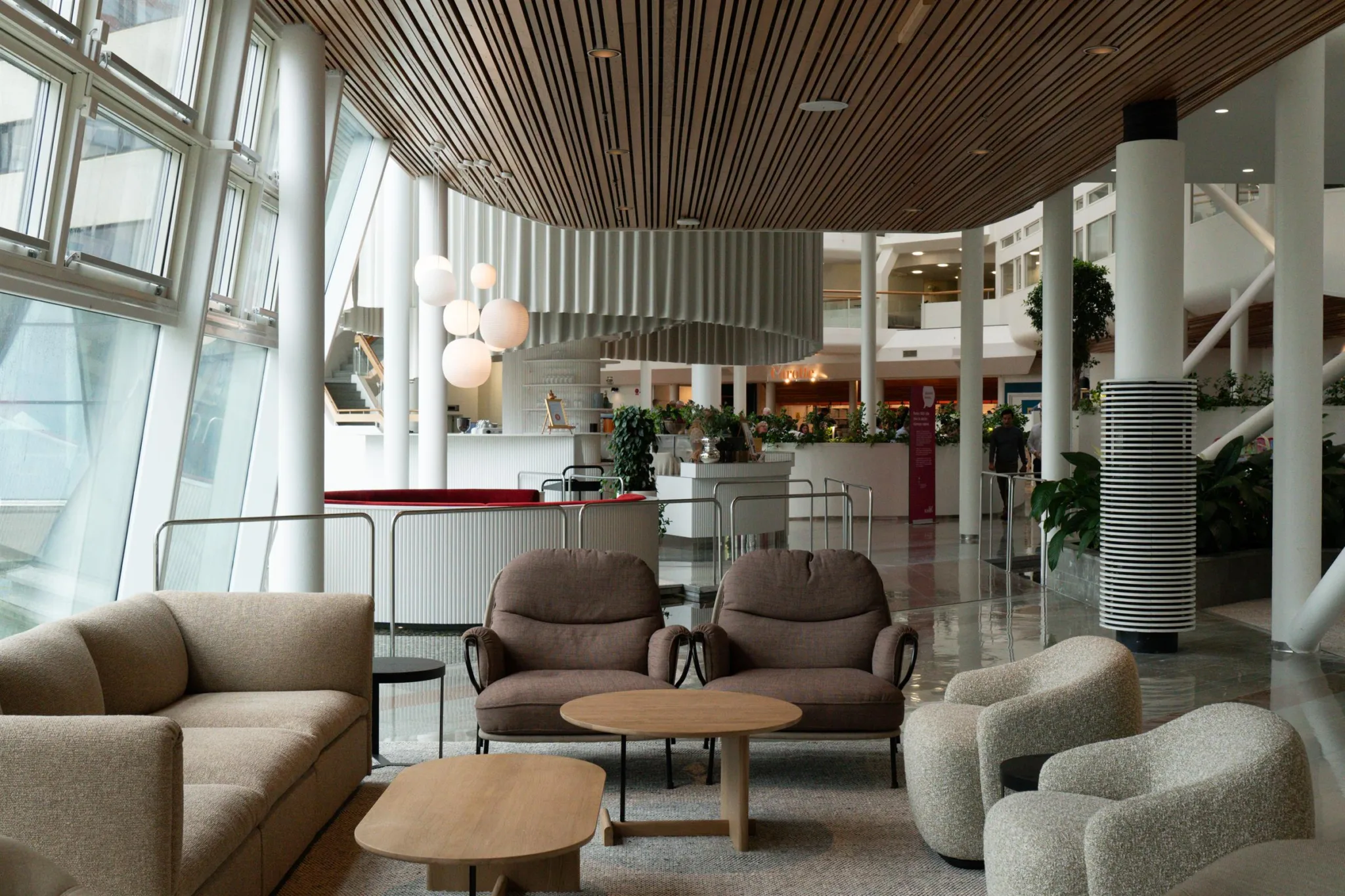1. En modern loungemiljö med soffor, fåtöljer, soffbord och ett tak av träpaneler i ljusa färger.