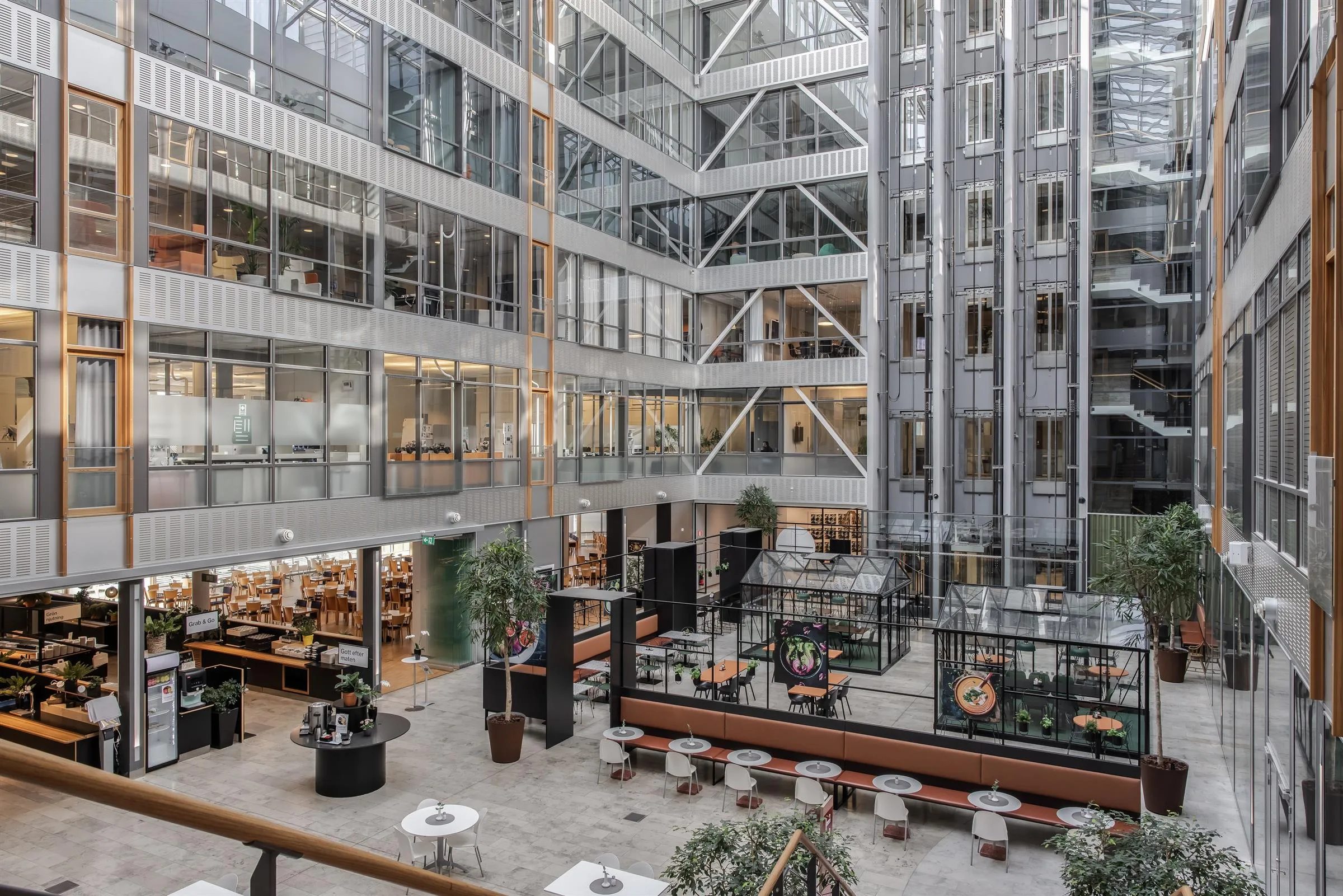 Ett ljust atrium med flera våningar, sittplatser, växter och glasväggar som omger kontorslokaler.