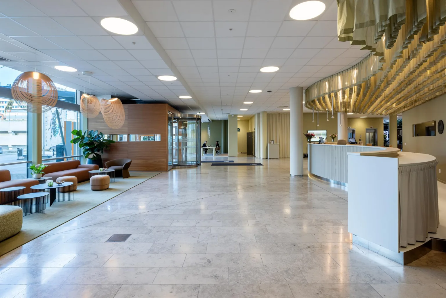En ljus och rymlig reception med marmorgolv, sittmöbler, växter och en receptionsdisk.