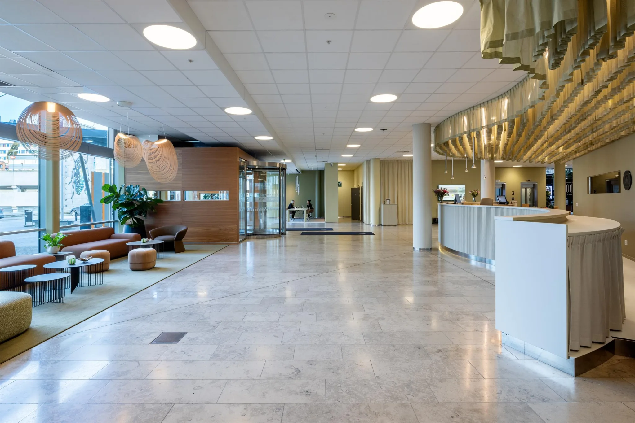 En ljus och rymlig reception med marmorgolv, sittmöbler, växter och en receptionsdisk.