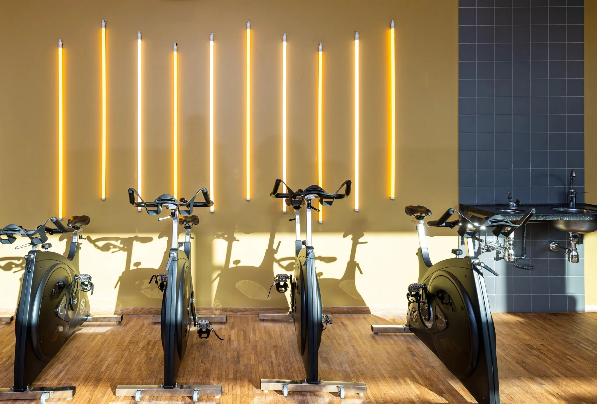 Cyklar för spinning står uppradade i ett rum med gul vägg och vertikala ljustuber.