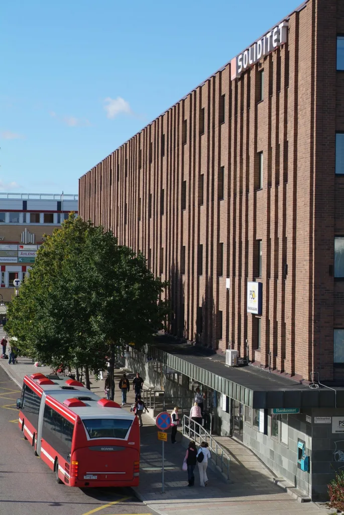 En brun tegelbyggnad med en buss på gatan och människor som promenerar.