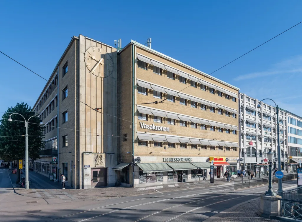 En gul byggnad med flera våningar och butiker vid en korsning under en molnfri himmel.
