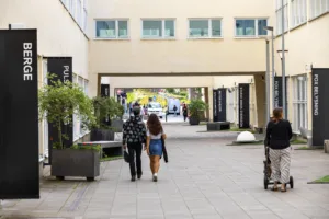 En gångväg mellan byggnader med två personer som går tillsammans och planteringslådor längs sidorna.