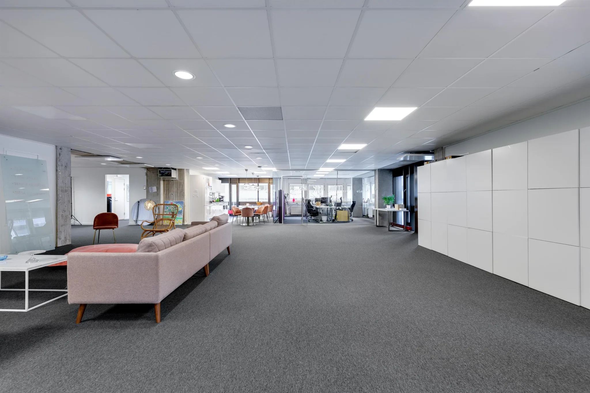 Ett rymligt kontorsutrymme med en rosa soffa och flera arbetsområden.