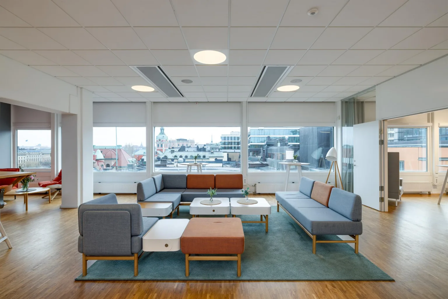 1. En modern sittgrupp med soffor och bord i ett ljust rum med stora fönster som visar en stadsvy.