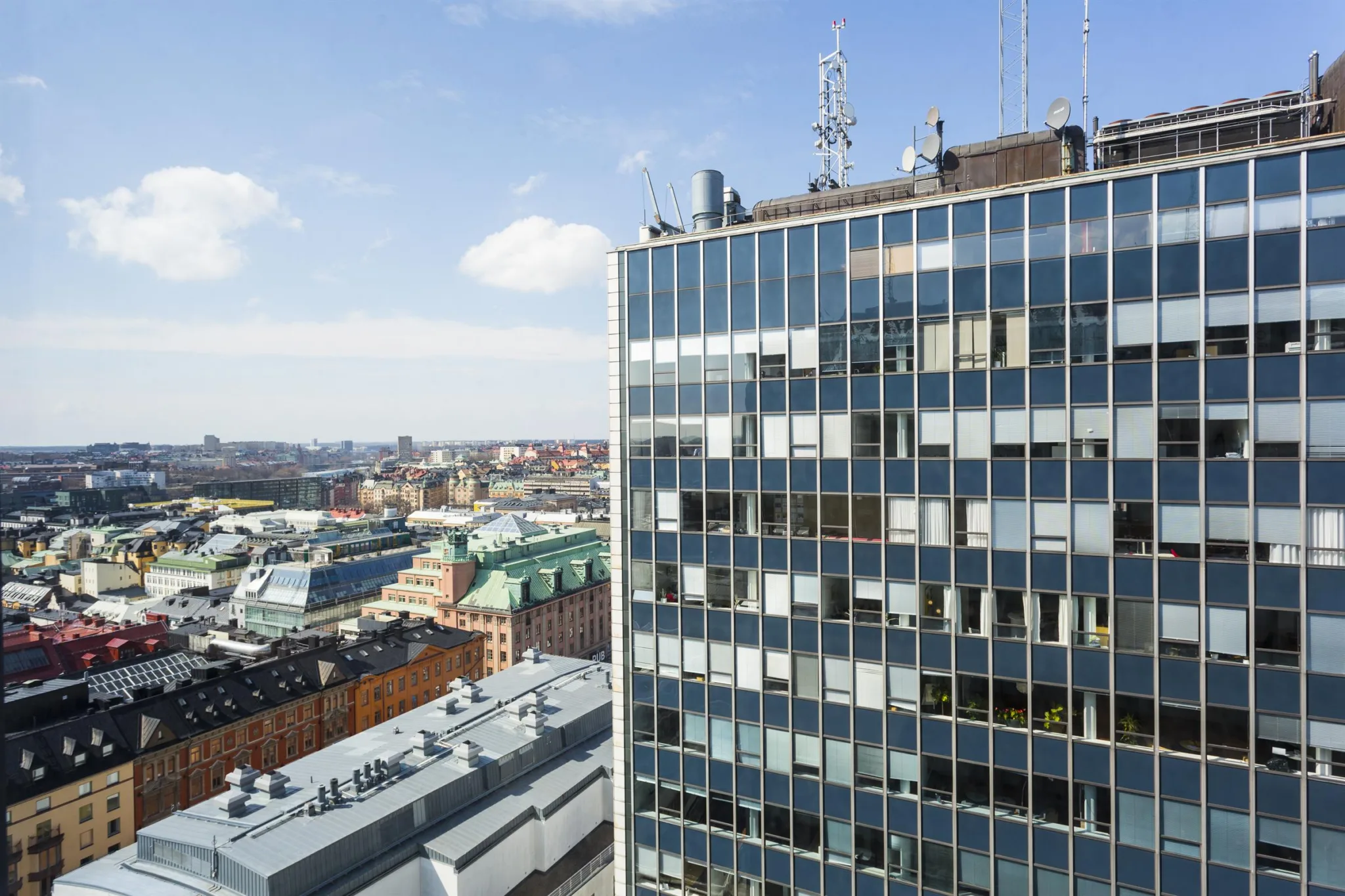 Höghus med glasfasad, antenner på taket och stadsutsikt i bakgrunden.