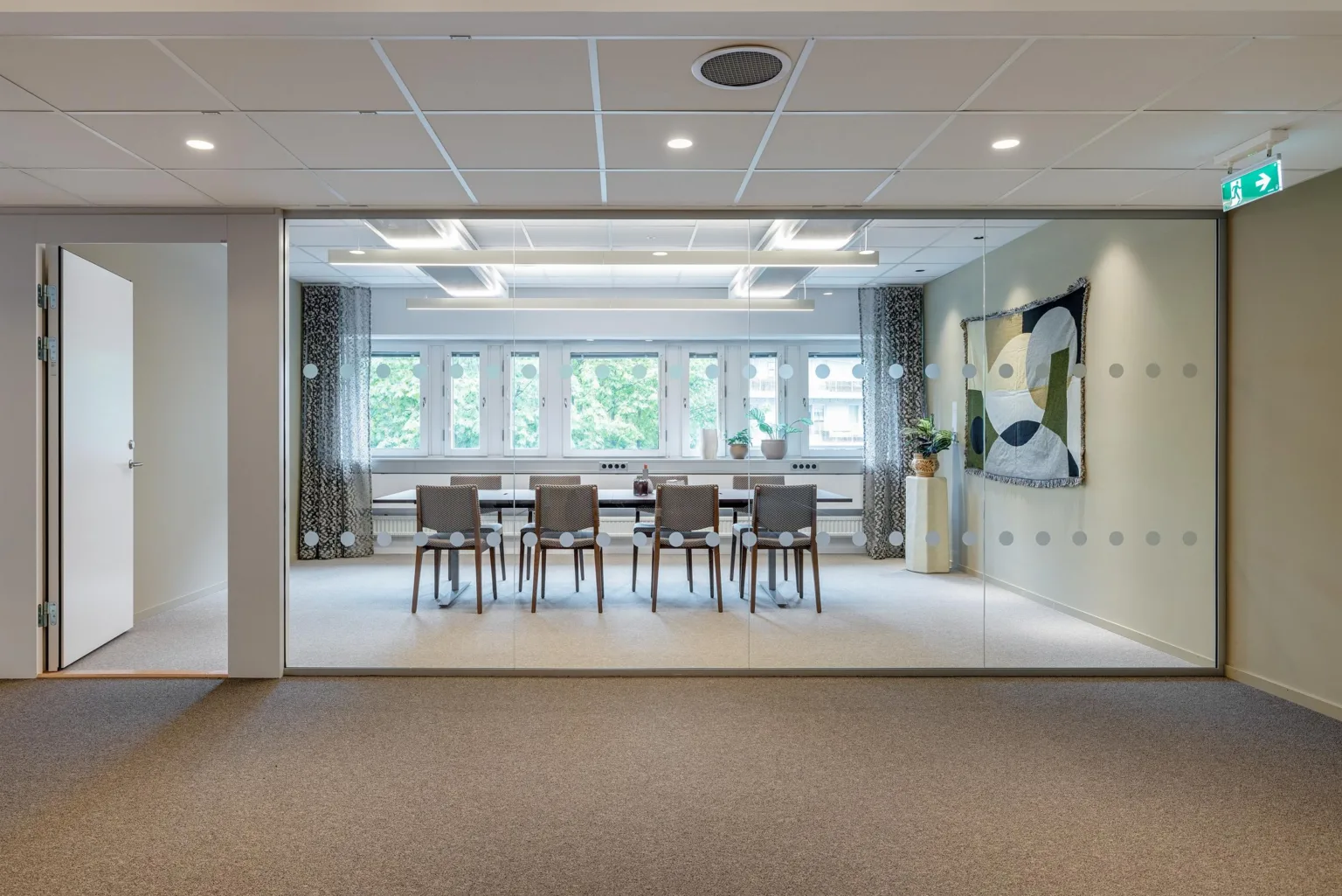 Ett modernt konferensrum med ett glasparti, ett långt bord, stolar och konst på väggen.