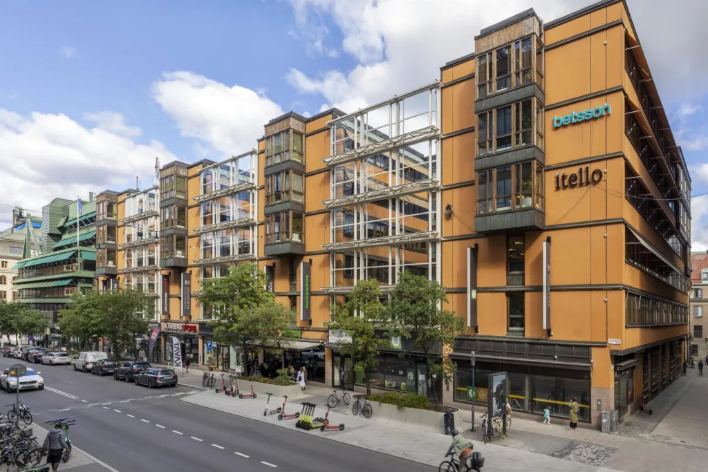 En rad av orangefärgade byggnader med glasdetaljer och butiker längs en stadsgata.